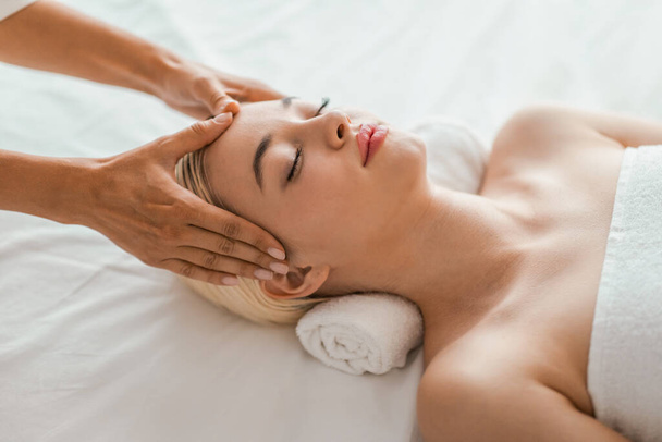 Un ambiente termale sereno in cui una giovane donna bionda riceve un delicato massaggio facciale, promuovendo un senso di relax e benessere - Foto, immagini