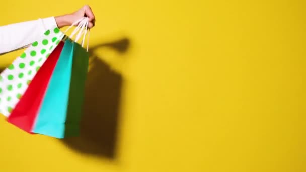 Vidéo Full HD du concept de shopping ou de vente. La main de la femme tient rouge, bleu et blanc sacs en papier tacheté isolé sur fond jaune vif. Vente bannière vidéo avec espace de copie. - Séquence, vidéo
