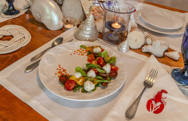 Смесь морепродуктов и капрезский салат с помидорами черри, моцареллой, базиликом и рукколой на красивой тарелке со столом для ракушек. - Фото, изображение