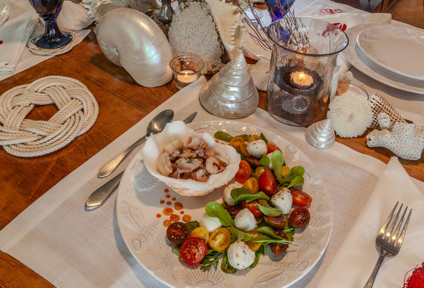 Mélange de fruits de mer et salade Caprese aux tomates cerises, mozzarella, basilic et roquette sur une belle assiette avec une table décor coquillage. - Photo, image