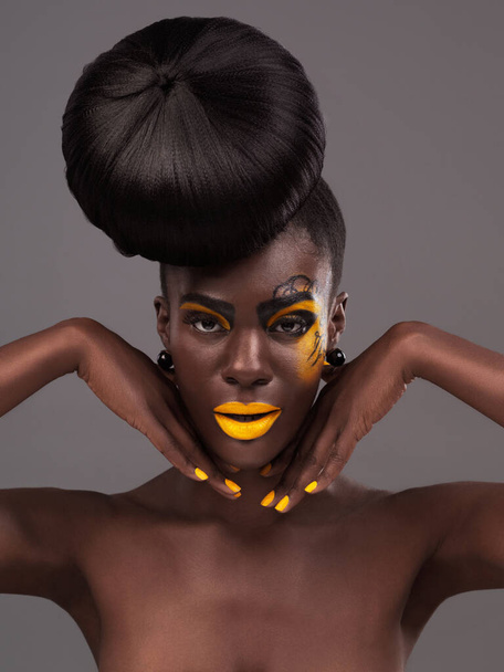 African, woman and studio portrait with makeup, beauty and creative yellow lipstick. Bold, model and skin with confidence, dramatic hair and bun for glamour and trendy cosmetics on grey background. - Photo, Image