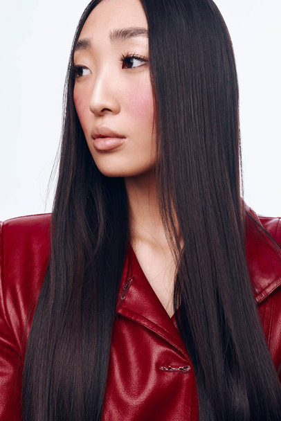Atrakcyjna Azjatka w czerwonej skórzanej kurtce z długimi czarnymi włosami, stojąca w czarnej koszuli - Zdjęcie, obraz