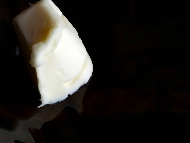 Egy darab fehér vaj egy sötét, tükörszerű felületen. fehéret a feketére. Fény a sötétben - Art Art with Food. - Fotó, kép