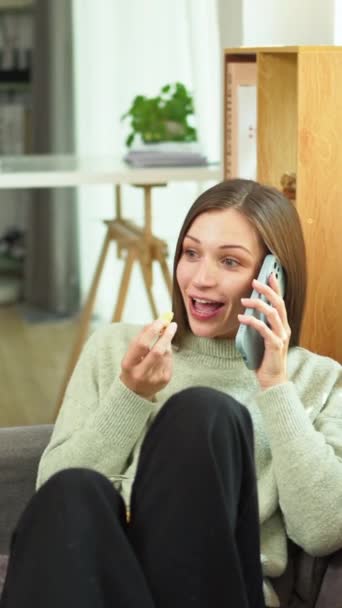 Gyönyörű fiatal nő, aki elégedett telefonos beszélgetés állomás, miközben ül a kanapén otthon. - Felvétel, videó