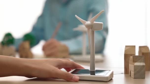 Empresaria mantenga modelo molino de viento representado utilizando energía limpia. Bloque de madera simboliza la casa de la ecología y el gráfico de poder verde se dispersan por la mesa, hombre de negocios que trabaja en el ordenador portátil. Delineación. - Imágenes, Vídeo