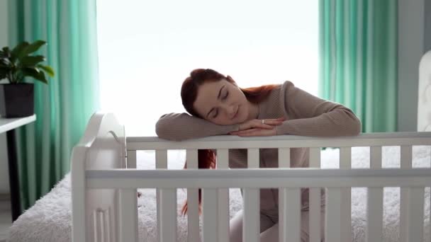 A fáradt fiatal anya elaludt támaszkodva az ágy, ahol az újszülött baba fekszik. Az anyaság fogalma. Anya szülési szabadságon van. Az újszülött gondozásának koncepciója. Lassú mozgás.. - Felvétel, videó