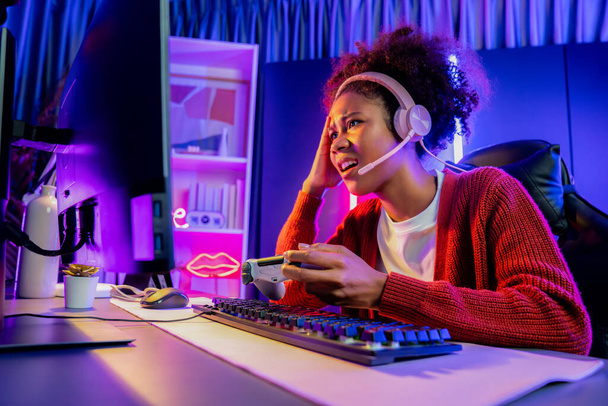 Afro-Amerikaanse meisje streamer teleurgesteld spelen online vechten met Esport ervaren team het dragen van een koptelefoon in neon kamer. Praten met andere spelers planing strategieën om concurrenten te winnen. Smaakstof. - Foto, afbeelding