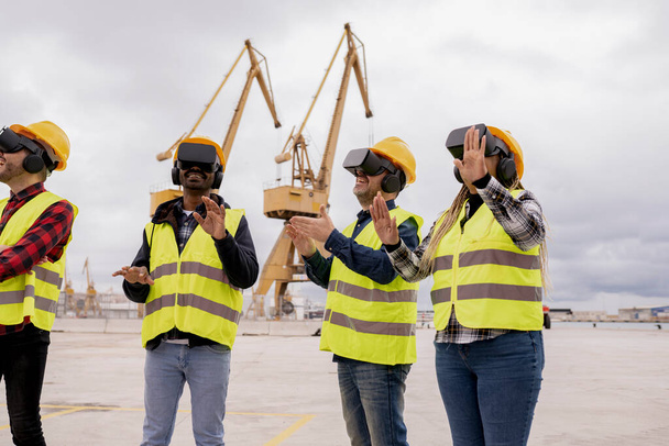 Quattro operai edili in cuffie VR impegnati in un progetto digitale su un grande sito industriale, dimostrando lavoro di squadra e integrazione tecnologica. - Foto, immagini