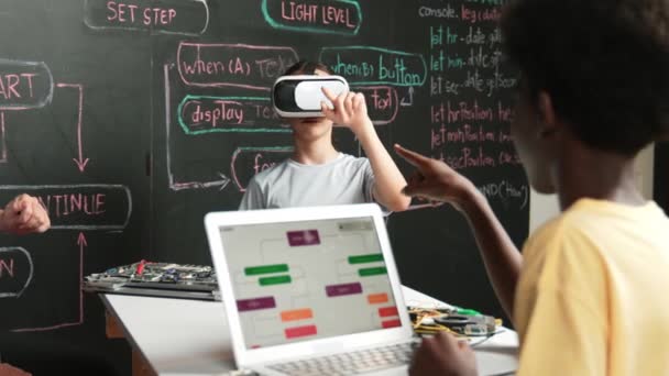 Afrikaanse jongen programmeren systeem terwijl Kaukasisch meisje invoeren metaverse terwijl zitten op blackboard met engineering code geschreven.high school meisje dragen VR of headset in STEM-technologie. Edificatie - Video