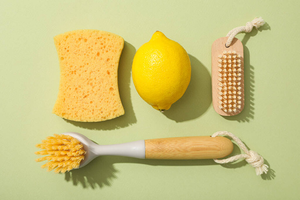 Brushes, sponge and lemon on green background, top view - Photo, Image