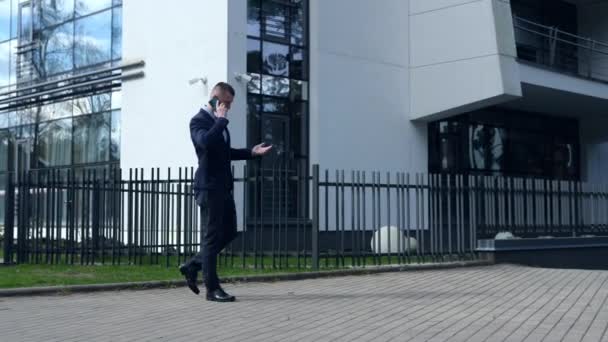 Obchodník, který telefonuje od telefonu k uchu, sebevědomě kráčí přes rám s pozadím kancelářské budovy. Podnikatel při chůzi vyjadřuje naléhavost. Dialog podnikatelů odráží rozhodnost  - Záběry, video