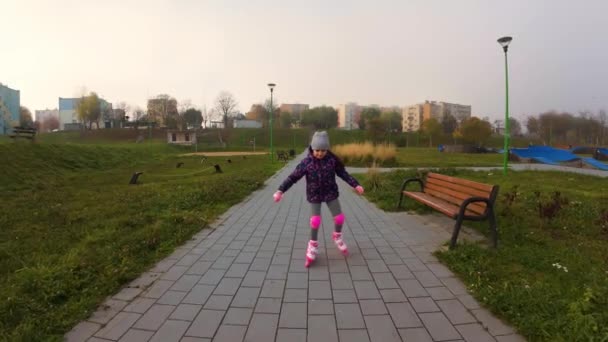 Ocho años niña aprendiendo a patinar al aire libre en el parque de la ciudad. Niño disfrutando del deporte activo, vista panorámica. Hermosa y saludable colegiala montando patines en el parque - Metraje, vídeo