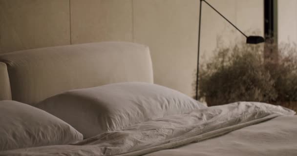 Klidná ložnice s měkkými polštáři na luxusní posteli a stylovou moderní lampou, ideální pro domácí dekorace témat. Elegantní ložnice interiér s měkkými polštáři a moderní lampy - Záběry, video