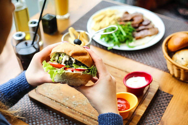 Человек держит сэндвич в руке, стоя перед тарелкой, наполненной различными видами пищи. - Фото, изображение