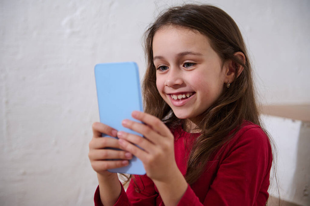 Nahaufnahme Porträt kaukasischen lächelnden glücklichen Kind Spaß auf dem Smartphone, mit mobilen Apps, spielen Online-Videospiele oder Filme ansehen Webinare oder Kinder Blogger, isoliert weißen Hintergrund - Foto, Bild