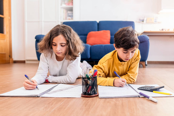 Двоє дітей пишуть у блокнотах, оточені олівцями та калькулятором, зосереджені на домашньому завданні. - Фото, зображення