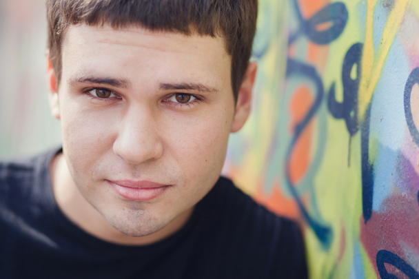 Attractive young man standing against colorful graffiti wall, close-up - Photo, Image