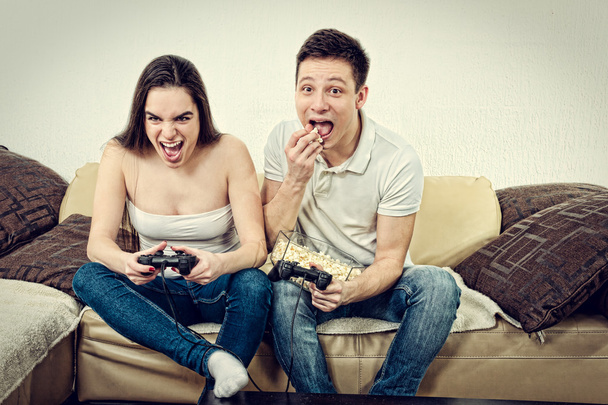 ζευγάρι στην αγάπη στον καναπέ κάθεται και παίζοντας βιντεοπαιχνίδια ζωής - Φωτογραφία, εικόνα