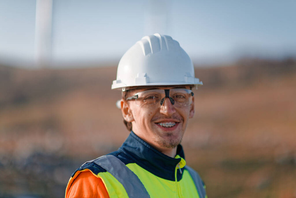 Een jonge ingenieur met gekruiste armen inspecteert een veld van windturbines en toont vertrouwen en toewijding aan duurzame energieprojecten. - Foto, afbeelding