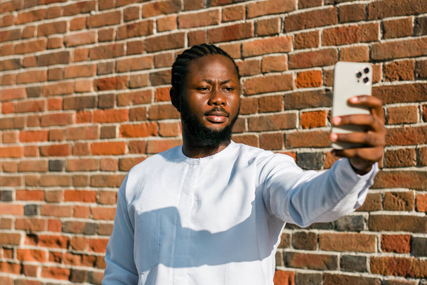 アフリカ系アメリカ人男性が夏のストリートカフェで携帯電話をチェック. ミレニアム世代とゲノムZの人々。 ソーシャルネットワークとデートアプリ - 写真・画像