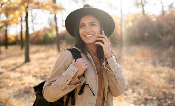 Eine hispanische Frau telefoniert während eines Spaziergangs in einem herbstlichen Park. Kopierraum - Foto, Bild