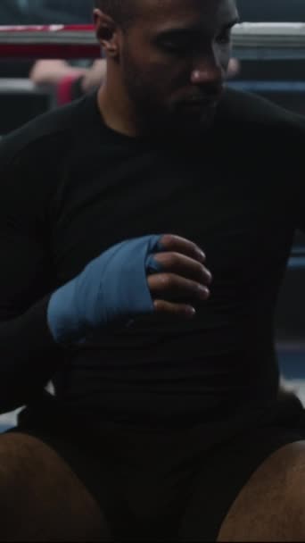 Afrikalı Amerikalı boksör dövüş sanatları için bandajla ellerini sarar ve boks eldivenleri giyer. Antrenör boks ringinde gençlerle yumruk antrenmanı yapıyor. Fiziksel aktivite ve yoğun çalışma. Dikey - Video, Çekim