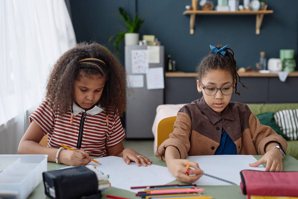 Portrait of two Black girls drawing pictures together sitting at table at home - Photo, Image