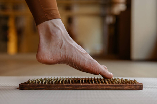 Los contornos de un pie explorando la aguda sensación de las clavijas de madera en una tabla de acupresión. - Foto, Imagen