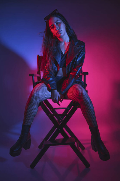A woman in a black jacket and black stockings sits in a chair - Photo, Image