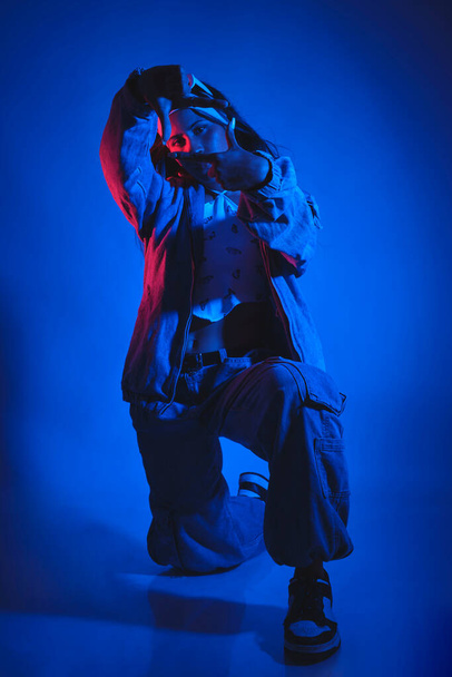 Egy kék kabátos és nadrágos férfi pózol egy fotón. A kék háttér és a manus ruha hűvös és feszült hangulatot kölcsönöz a képnek. Városi táncos koncepció - Fotó, kép