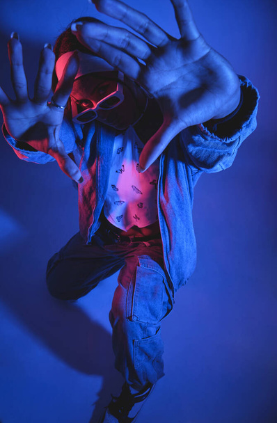 Un uomo in giacca blu e jeans sta posando per una foto con le mani in alto in aria. La foto è in una combinazione di colori blu e viola, dandogli un'atmosfera fresca e tagliente - Foto, immagini