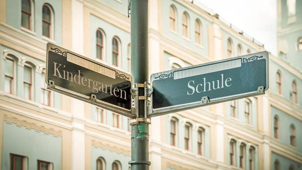 Un'immagine con un cartello che punta in due direzioni diverse in tedesco. Una direzione punta alla scuola, l'altra punta all'asilo.. - Foto, immagini