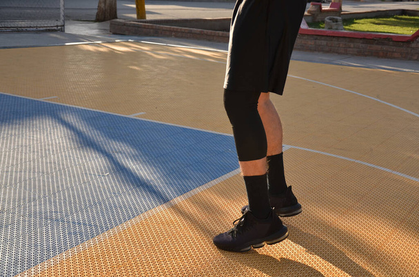 Siyah tişörtlü ve siyah çantalı genç bir kız şehirdeki basketbol sahasında duruyor. - Fotoğraf, Görsel