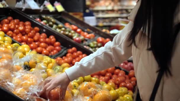 In de supermarkt selecteert de vrouw verse tomaten, zachtjes knijpen elk om te zorgen voor rijpheid. Ze vergelijkt zorgvuldig tomaten, en zorgt ervoor dat ze de meest sappige tomaten plukt voor haar maaltijden. - Video
