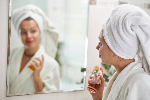 Femme en peignoir de bain appliquant un parfum sur son cou - Photo, image