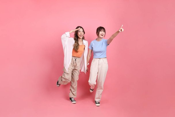 Freunde junger Erwachsener, ostasiatische Frauen der 20er Jahre, die auf den rosafarbenen Hintergrund zeigen.  - Foto, Bild