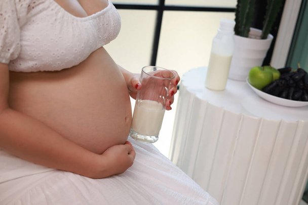 donna incinta che beve un bicchiere d'acqua e mangia vitamine a casa. Salute prenatale e idratazione - Foto, immagini