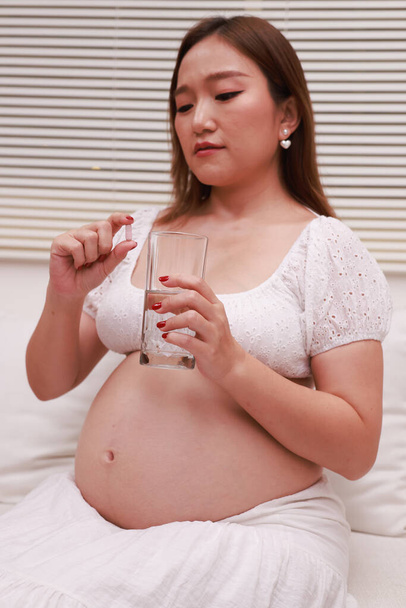donna incinta che beve un bicchiere d'acqua e mangia vitamine a casa - Foto, immagini