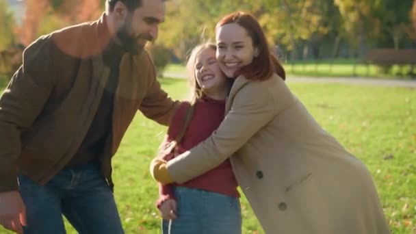Χαρούμενη Καυκάσια οικογένεια γελώντας αγκαλιάζοντας μαζί Σαββατοκύριακο διακοπών στο ηλιόλουστο πάρκο της πόλης γονείς μικρό παιδί κοριτσάκι κορίτσι αγκαλιά γέλιο χαμόγελο ασφάλεια δέσιμο επιμέλεια αγκαλιά υγιείς ανθρώπους παιχνίδι - Πλάνα, βίντεο