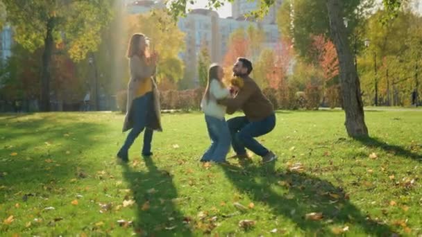 Caucasian happy family weekend holiday nature outdoors in city autumn park together loving father lift little child kid girl daughter spin turning whirl rotate around play fun game mother applauding - Footage, Video