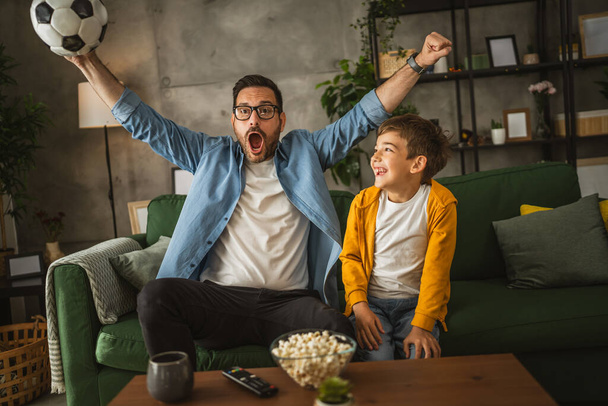 Padre e figlio caucasico guardare partita di calcio e tifare a casa rumoroso, eccitato, felice - Foto, immagini