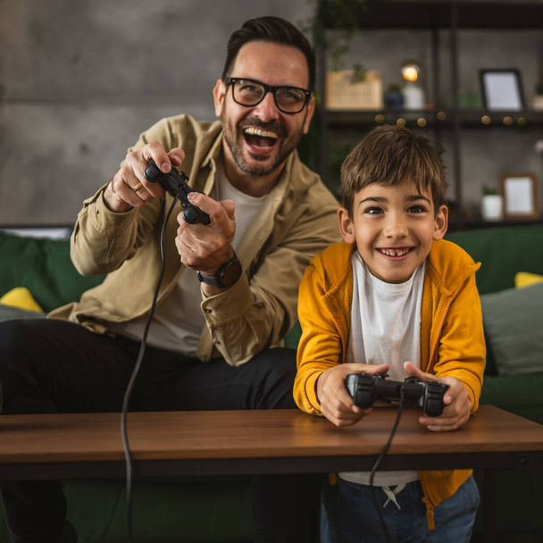 Father and son caucasian play video games with joystick and have fun at home happy enjoy - Photo, Image