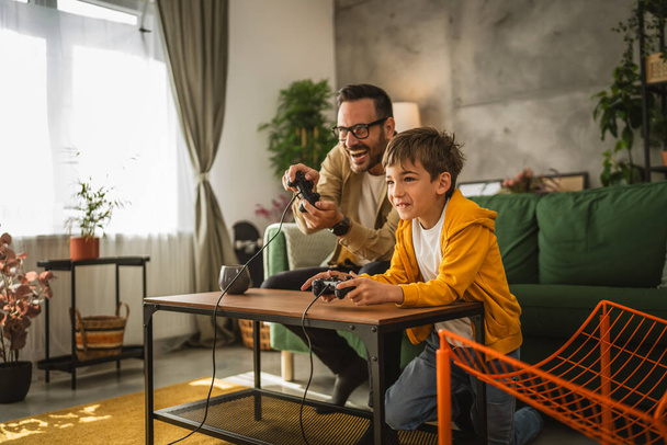 Отец и сын кавказский играть в видеоигры с джойстиком и весело провести время дома счастливо наслаждаться - Фото, изображение