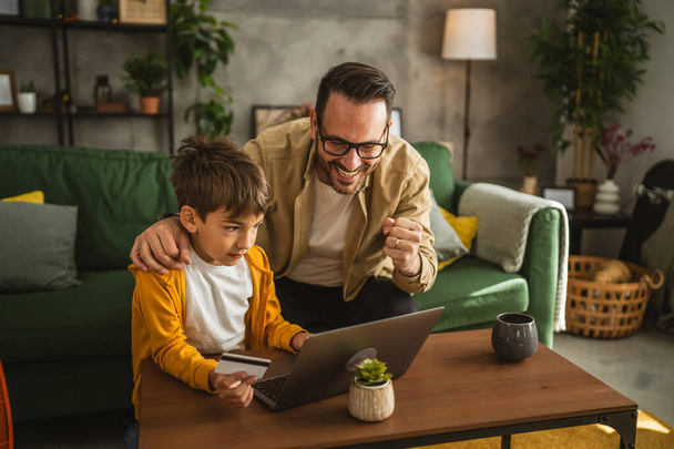 Ojciec i syn kaukaski kupić online z karty kredytowej na laptopie w domu - Zdjęcie, obraz