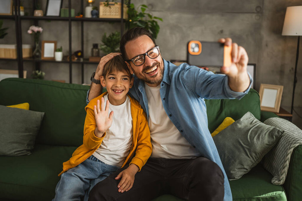 Vader en zoon maken een zelfportret in de woonkamer, gelukkig, samen - Foto, afbeelding