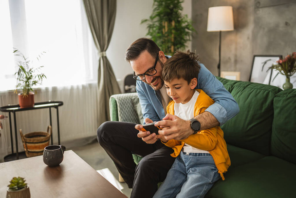 Vater und Sohn spielen Videospiele auf dem Handy und genießen zu Hause - Foto, Bild