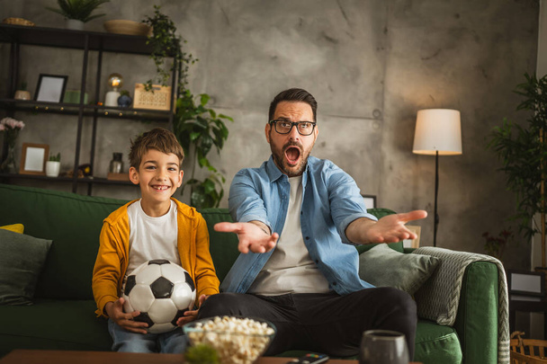 Vader en zoon Kaukasisch kijken voetbal wedstrijd en juichen thuis luidruchtig, opgewonden, gelukkig - Foto, afbeelding