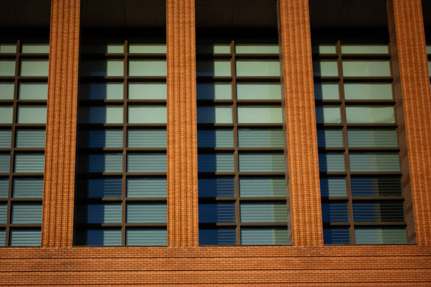 Lähikuva yksityiskohtaisesti modernin oranssi tiili rakennuksen julkisivu sinisellä sävytetty ikkunat. Toimiston lasiseinäkuvio. Kaupunkiarkkitehtuuri. Teollisuuden tyyli talo - Valokuva, kuva
