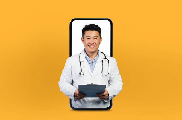Ασιάτης ώριμος άνθρωπος γιατρός παρέχει συμβουλές για την υγεία μέσω ενός smartphone, στέκεται μέσα στην οθόνη σε ένα γαλήνιο και επαγγελματικό περιβάλλον - Φωτογραφία, εικόνα