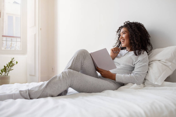 La donna ispanica è seduta su un letto, assorta nella lettura di un libro. Tiene il libro tra le mani, con un'espressione concentrata sul viso - Foto, immagini